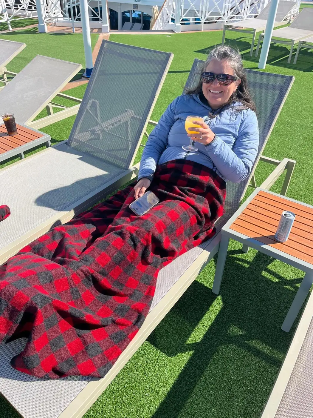 Denise, 52, smiling in sunglasses relaxing outdoors on a lounge chair