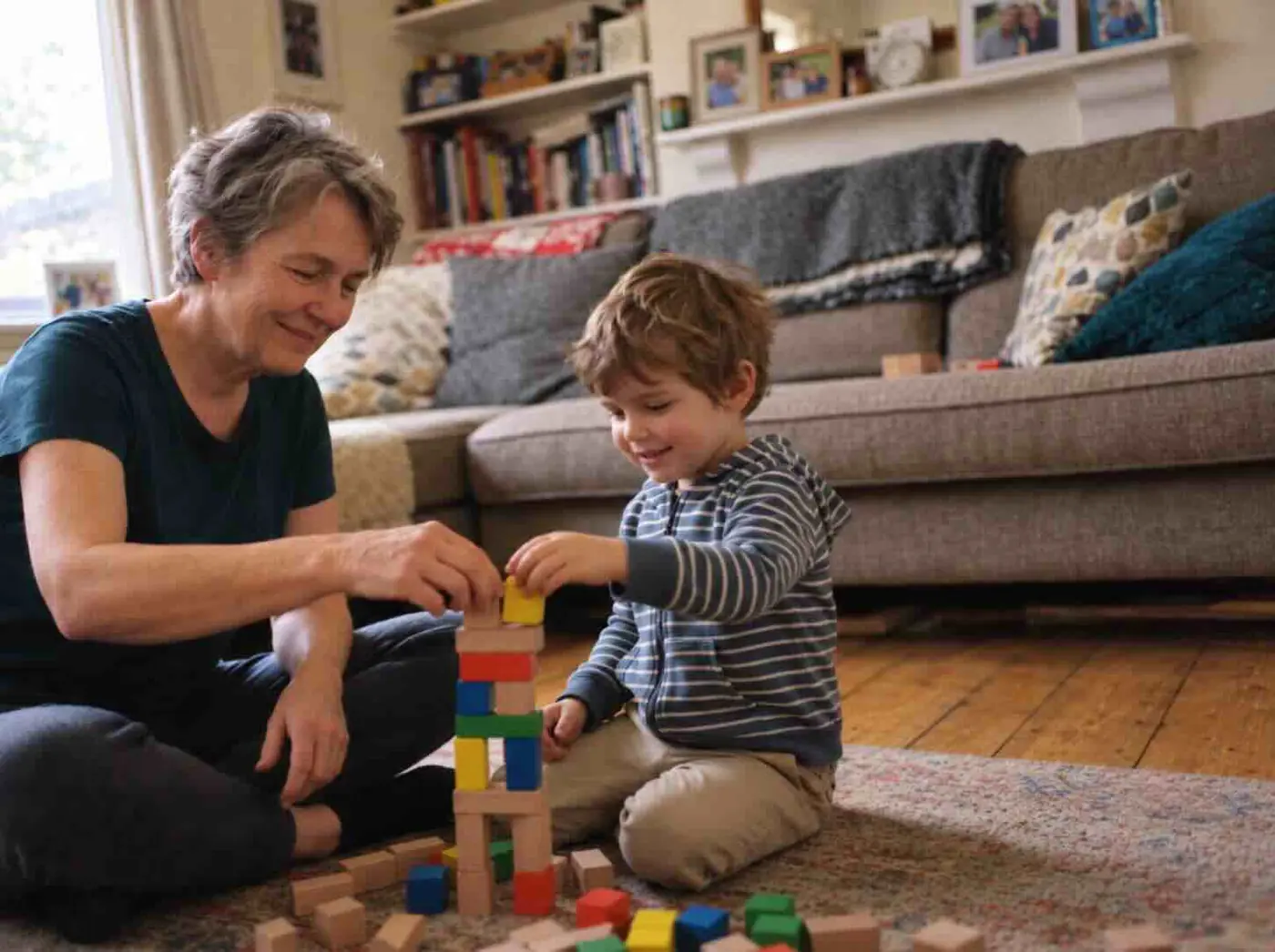 Marion, 64, sitting on the wooden floor playing with wooden building blocks with her grandson