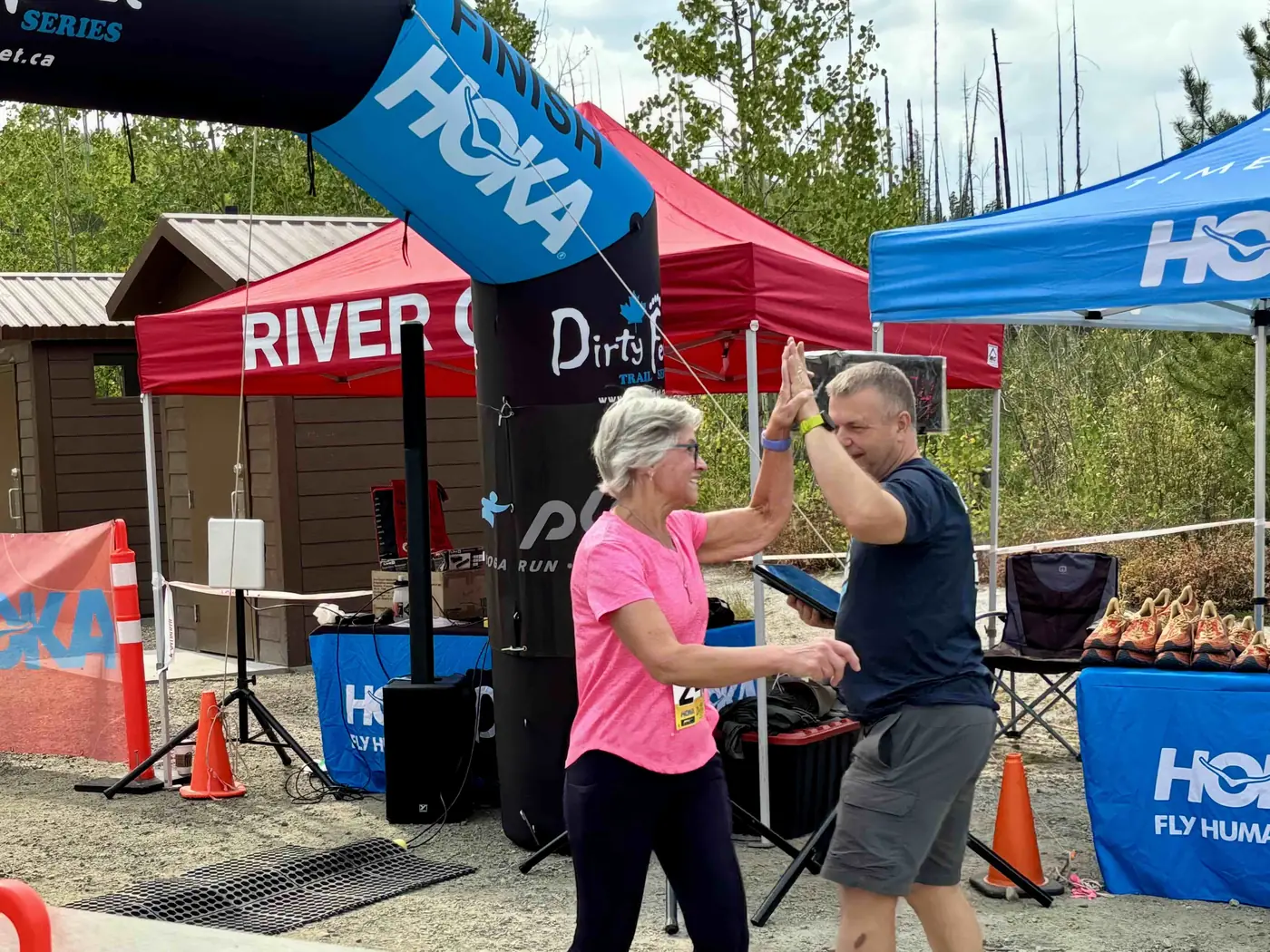 A woman in a bright pink shirt joyfully high-fiving a supporter at a trail race finish line arch